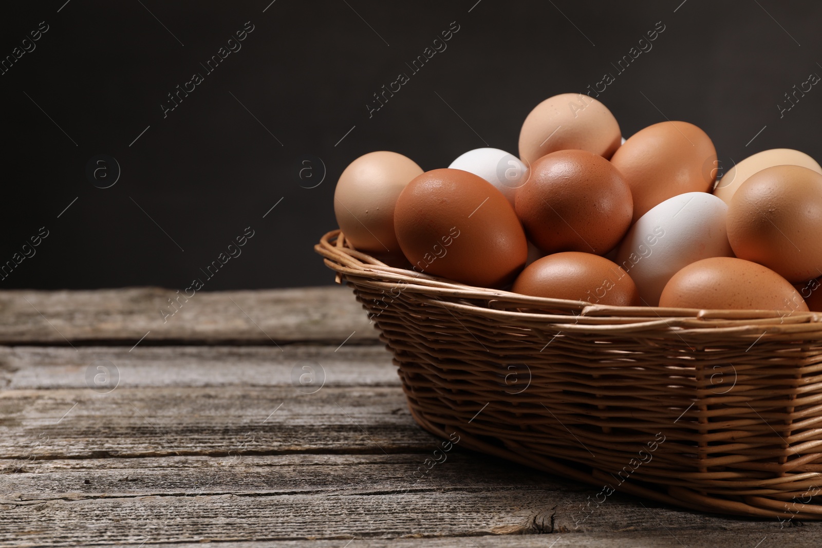 Photo of Fresh chicken eggs in wicker basket on wooden table. Space for text