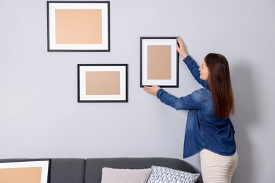 Woman hanging picture frame on gray wall indoors