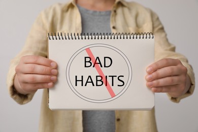 Image of Woman holding notebook with prohibited symbol and phrase Bad Habits against light background, closeup