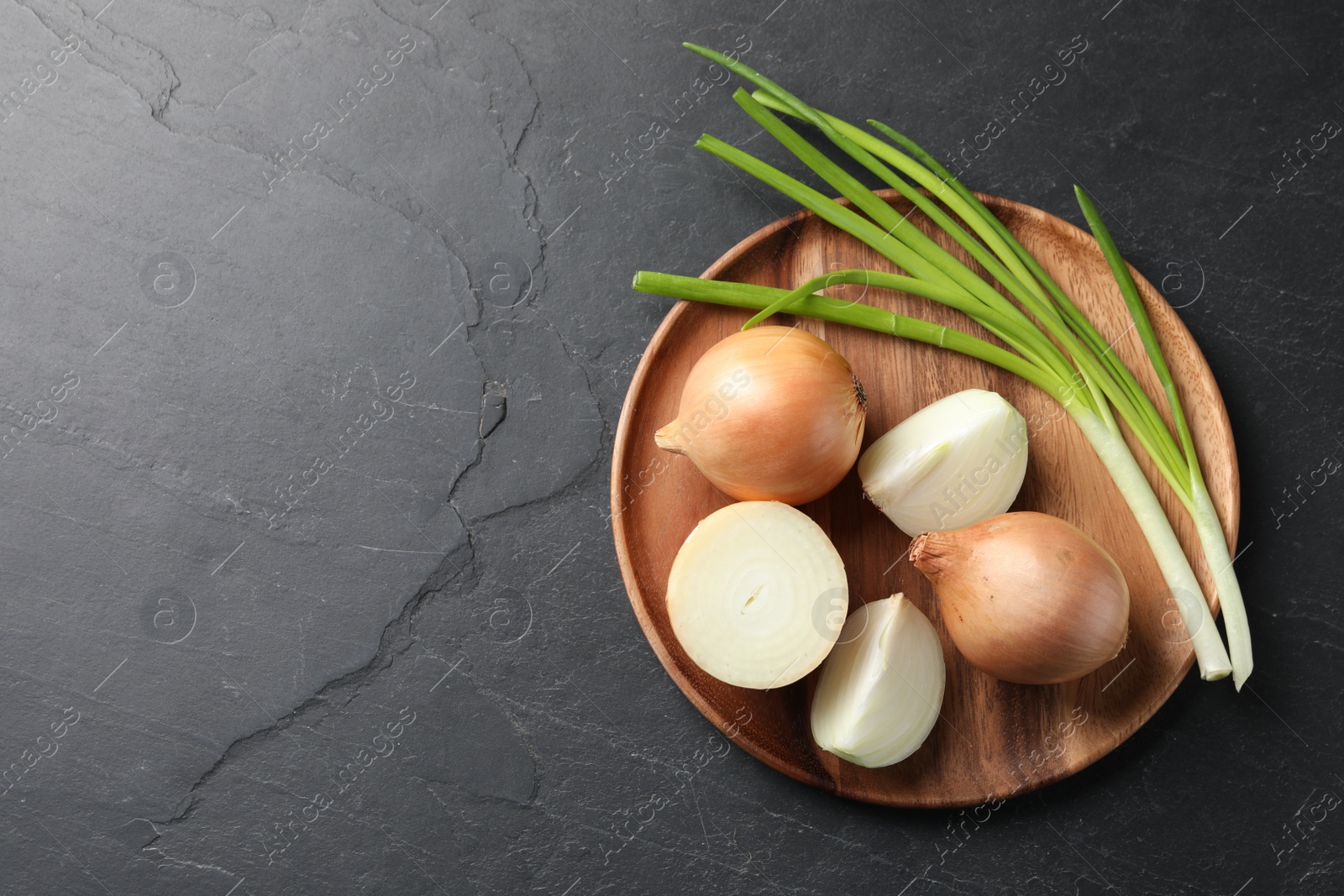 Photo of Different sorts of onion on black textured table, top view. Space for text