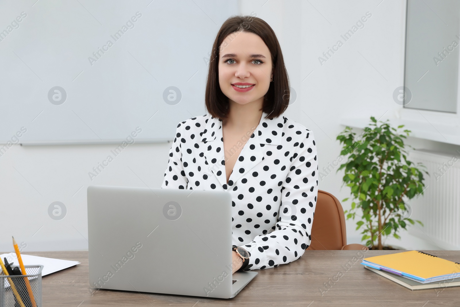 Photo of Happy young intern working with laptop at table in modern office