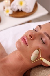 Photo of Young woman receiving facial massage with jade roller in beauty salon, closeup