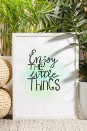 Photo of Frame with words Enjoy The Little Things near houseplants on carpet