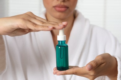 Photo of Woman with bottle of cosmetic serum on light background, closeup