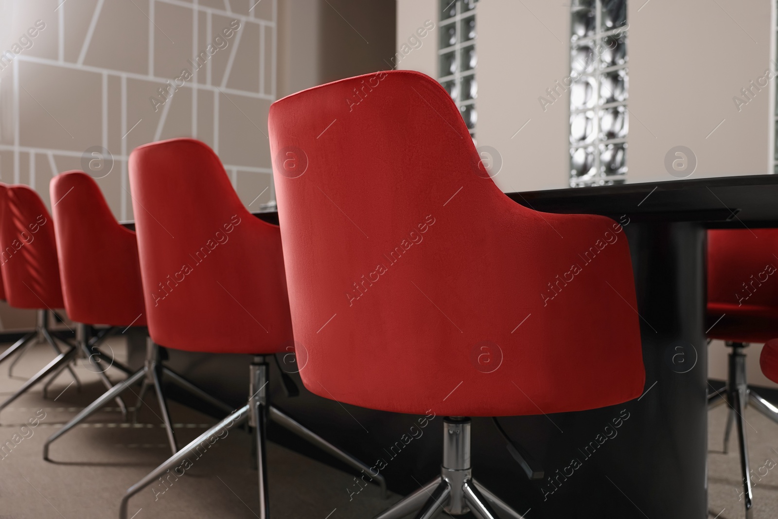 Photo of Stylish red office chairs and large table in empty conference room