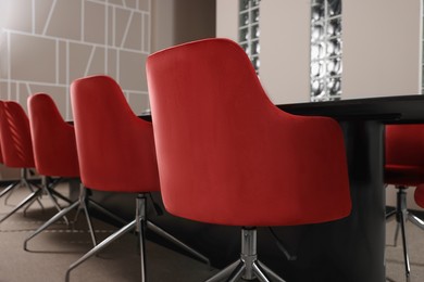 Photo of Stylish red office chairs and large table in empty conference room