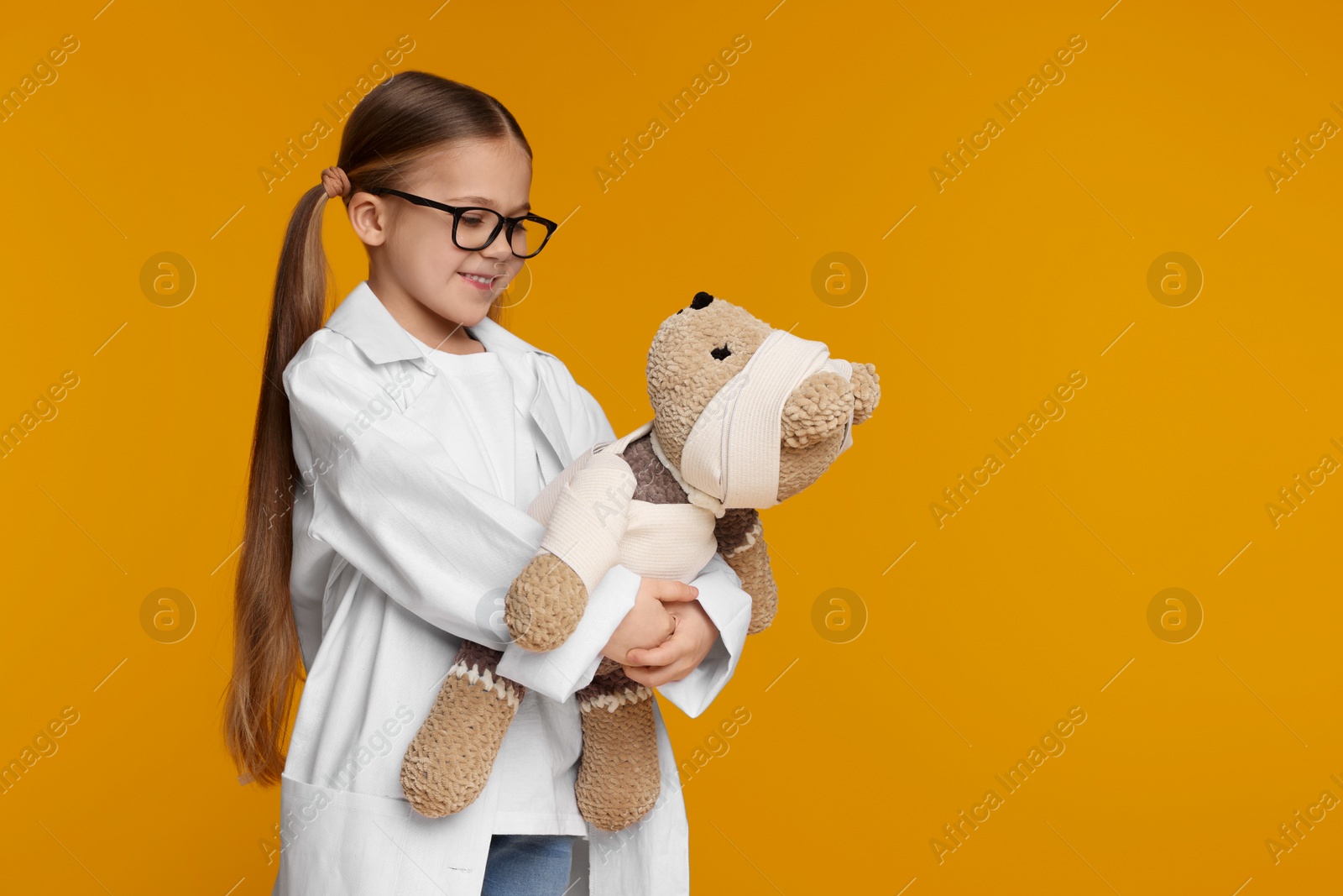 Photo of Little girl in medical uniform with toy bear on yellow background. Space for text