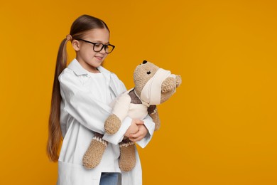 Photo of Little girl in medical uniform with toy bear on yellow background. Space for text