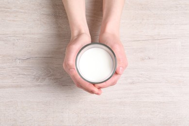 Photo of Woman holding glass of milk at white wooden table, top view