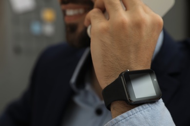 Photo of Businessman wearing smart watch and talking on smartphone in office, closeup