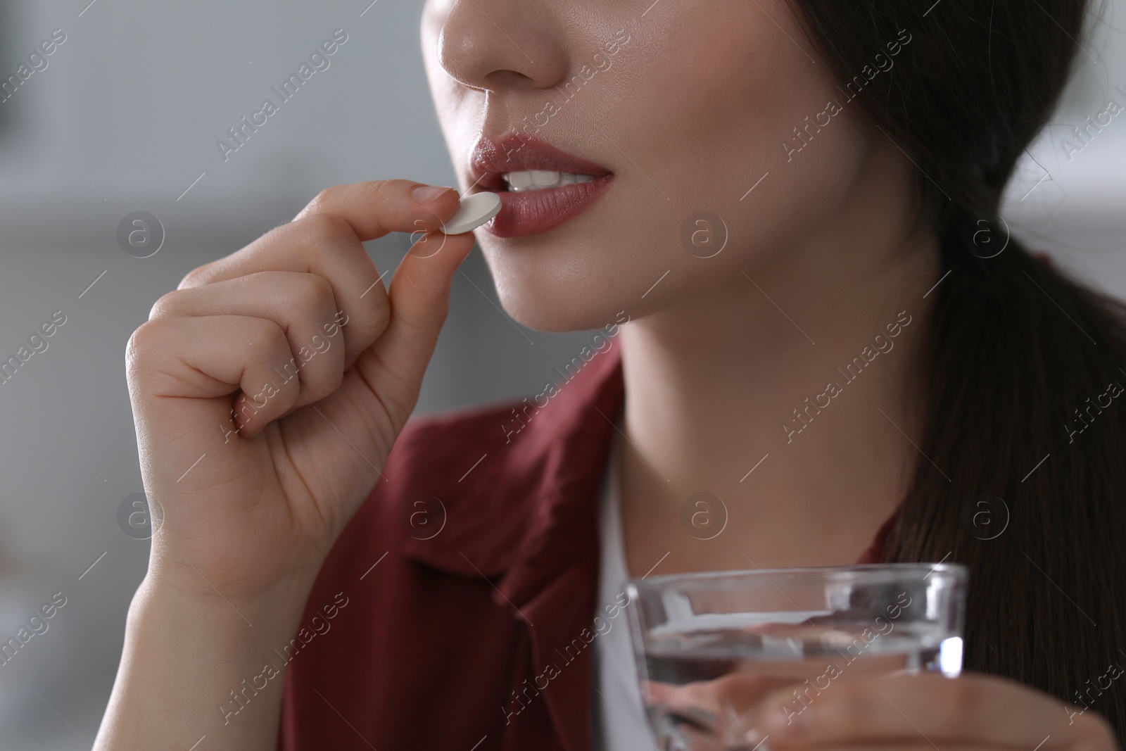 Photo of Woman with glass of water taking antidepressant pill on blurred background, closeup