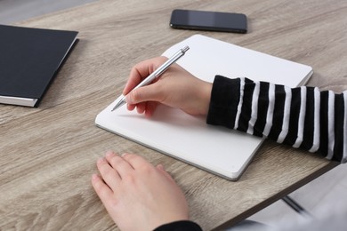 Photo of Woman writing in notebook at wooden table, closeup