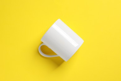 Photo of One white ceramic mug on yellow background, top view