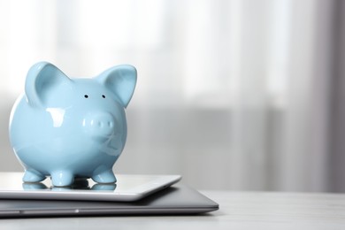 Photo of Piggy bank, tablet and laptop on white table indoors. Space for text