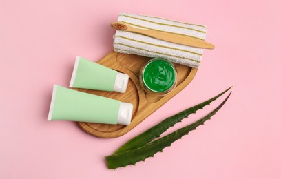 Photo of Tubes of toothpaste, fresh aloe, toothbrush and towel on pink background, flat lay