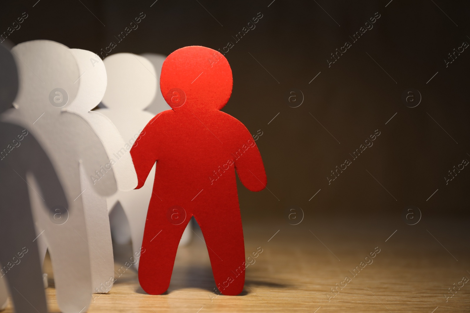 Photo of Red human paper figure standing out from white ones on wooden table, space for text. Responsibility concept