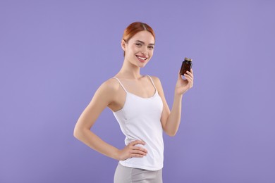 Happy young woman with bottle of pills on purple background. Weight loss