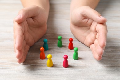 Photo of Woman protecting colorful pawns at white wooden table, closeup. Social inclusion concept