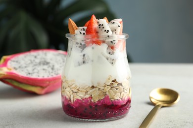 Photo of Glass jar of granola with pitahaya, yogurt and strawberries on white table