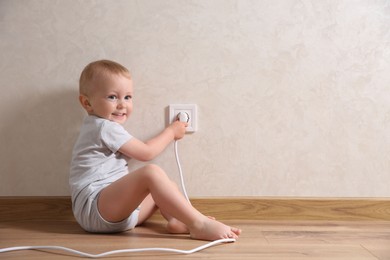 Photo of Little child playing with electrical socket and plug indoors, space for text. Dangerous situation