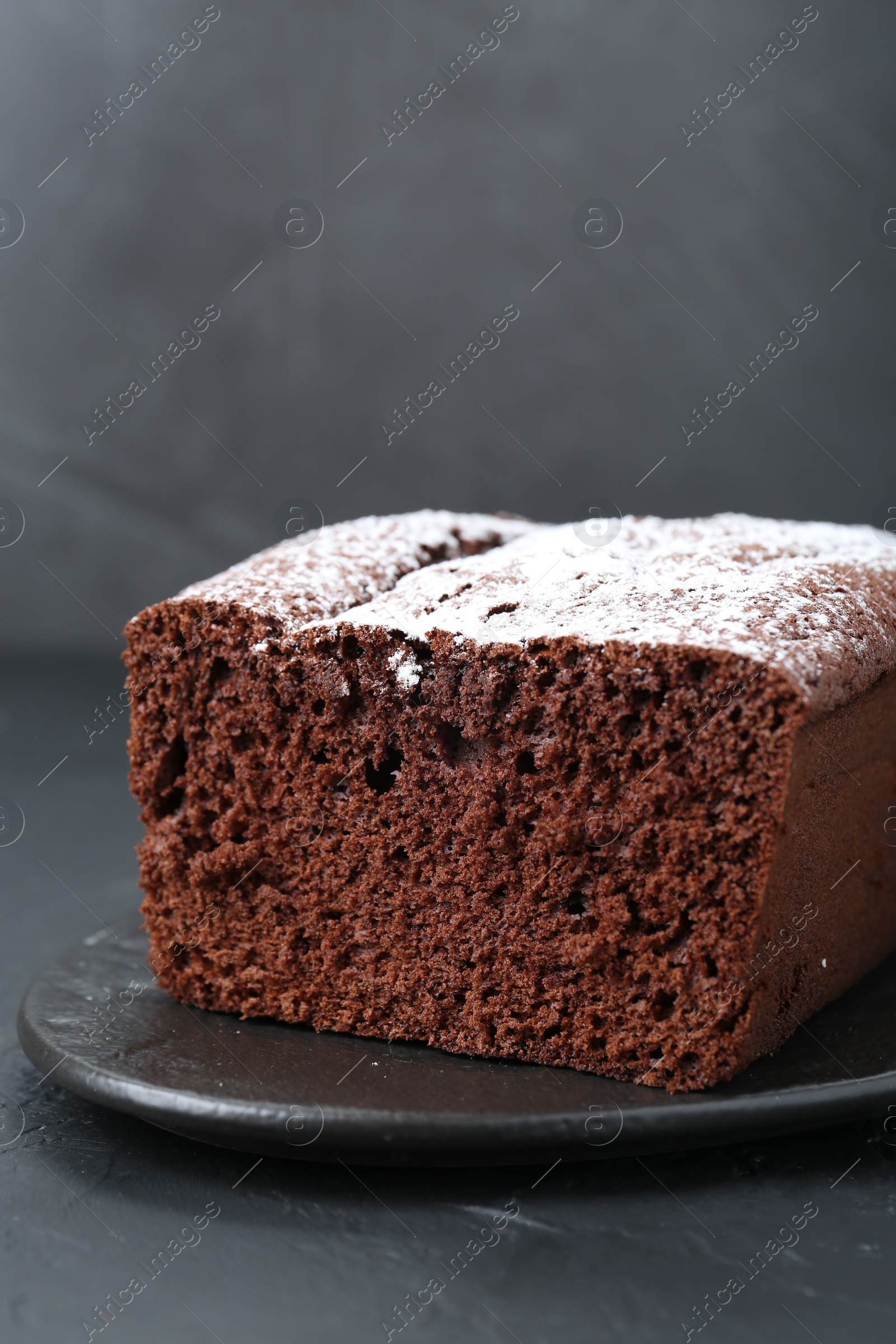 Photo of Tasty chocolate sponge cake with powdered sugar on black table, closeup