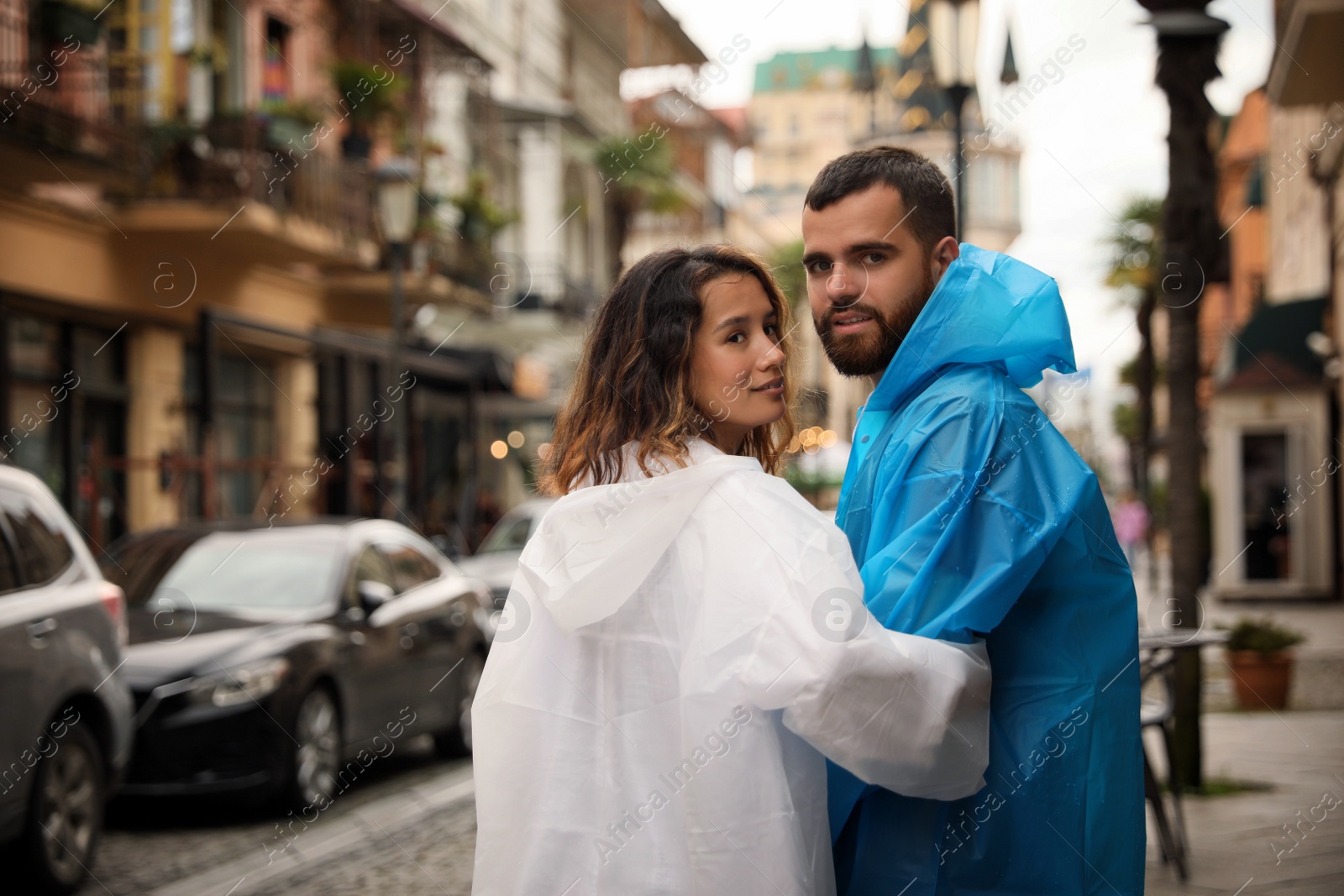 Photo of Young couple in raincoats enjoying time together on city street