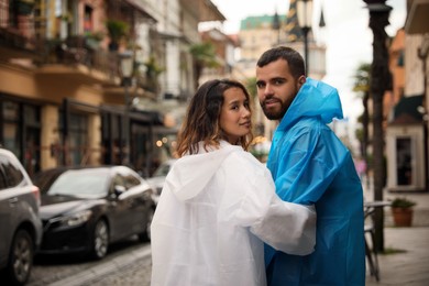 Photo of Young couple in raincoats enjoying time together on city street