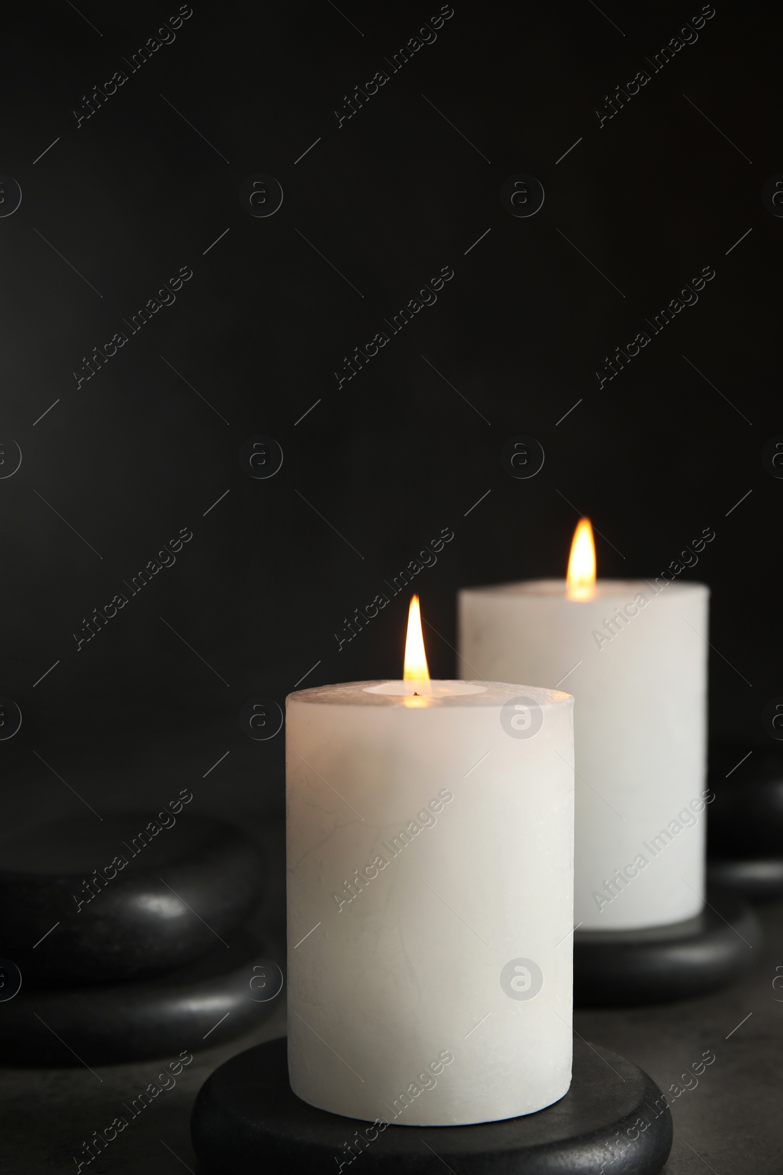 Photo of Burning candles and black spa stones on grey table, space for text