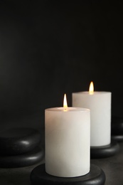 Photo of Burning candles and black spa stones on grey table, space for text