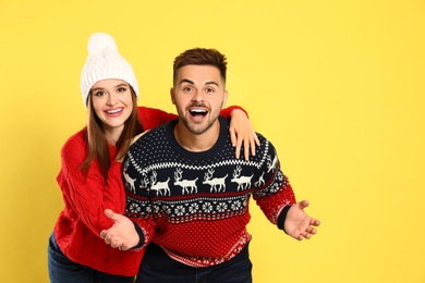 Couple wearing Christmas sweaters on yellow background