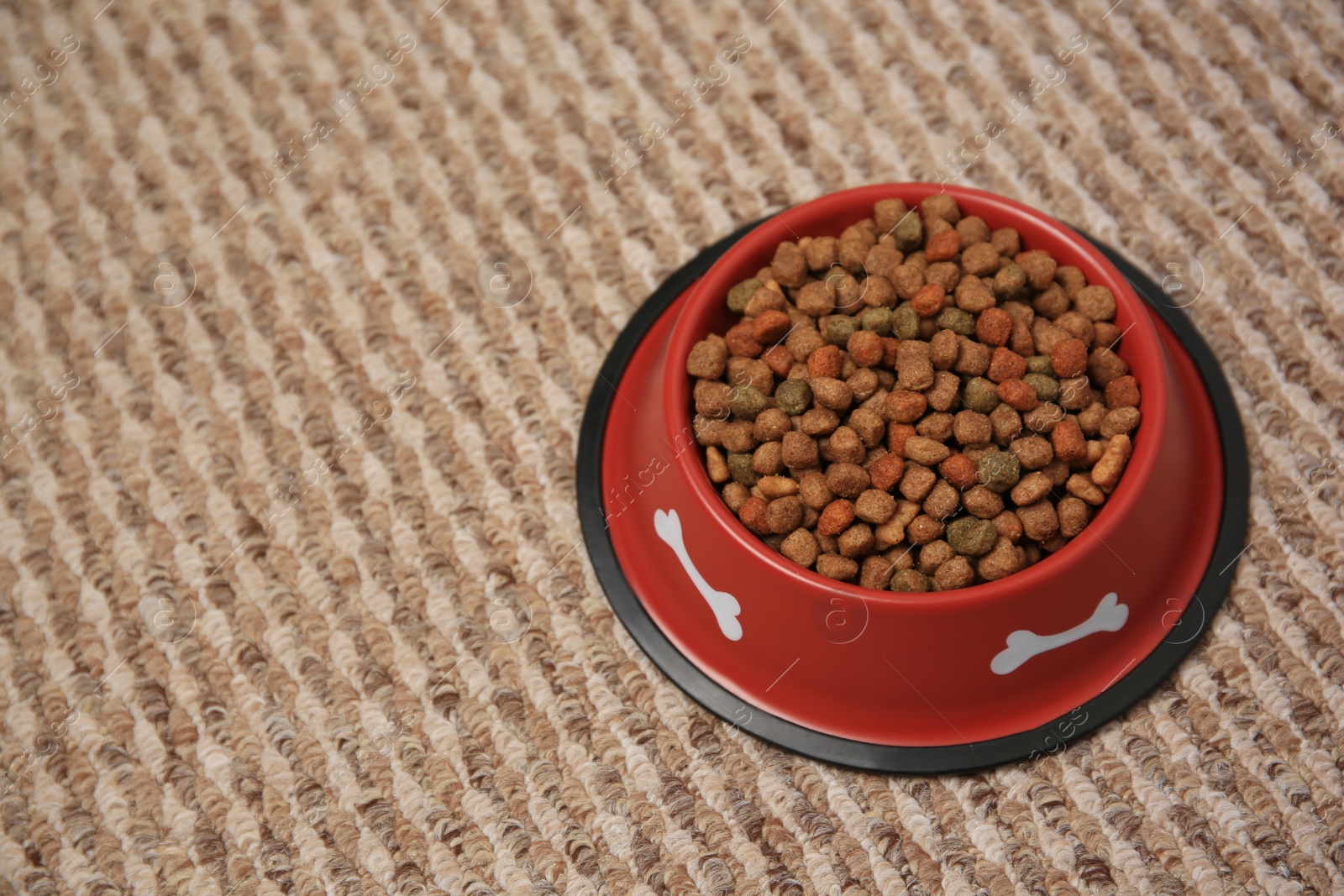 Photo of Dry dog food in feeding bowl on soft carpet. Space for text