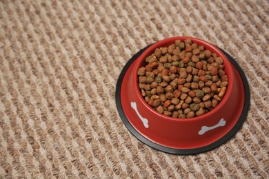 Photo of Dry dog food in feeding bowl on soft carpet. Space for text