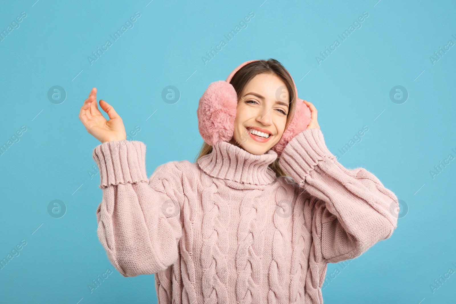 Photo of Happy woman wearing warm earmuffs on light blue background