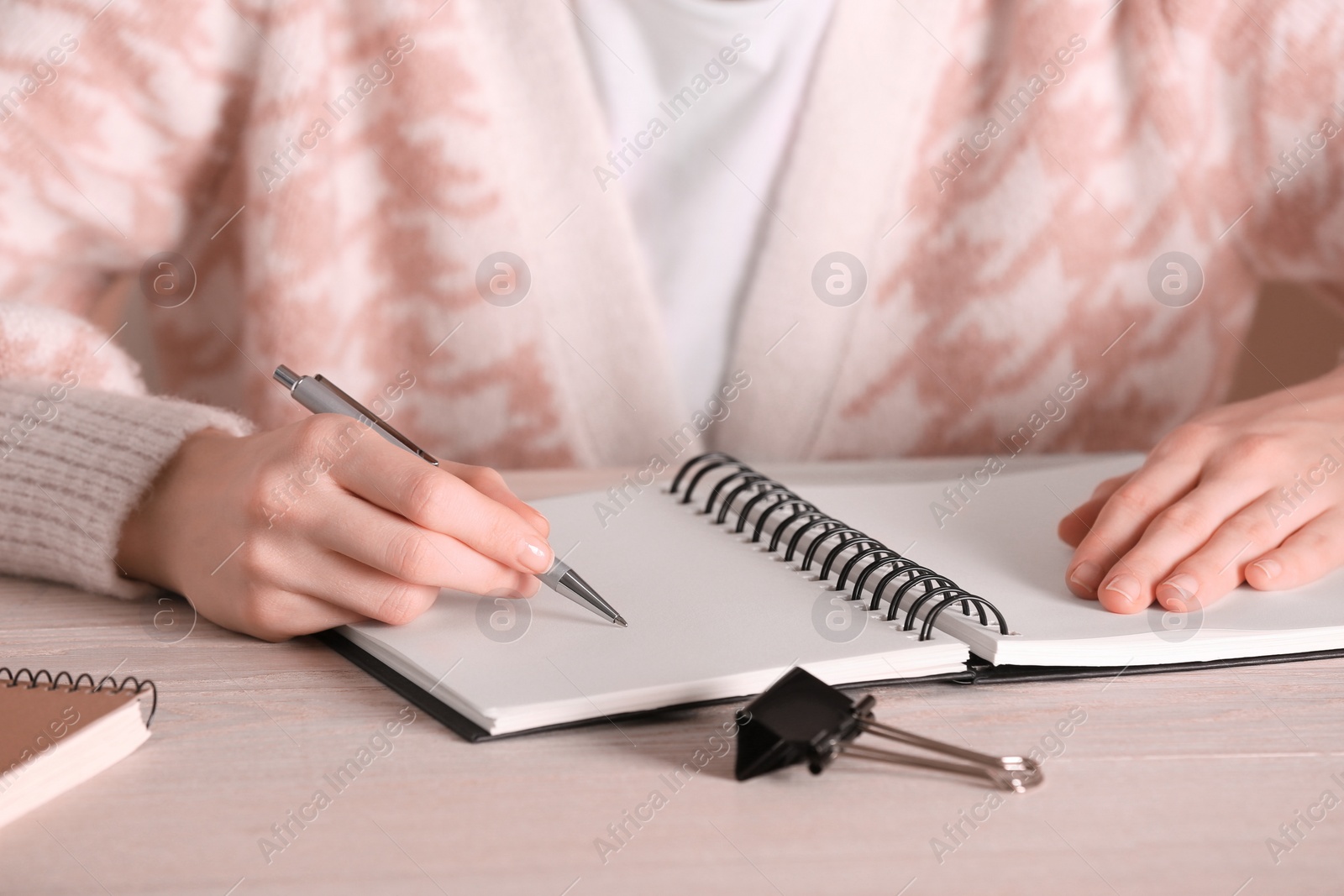 Photo of Woman writing in notebook at white wooden table, closeup