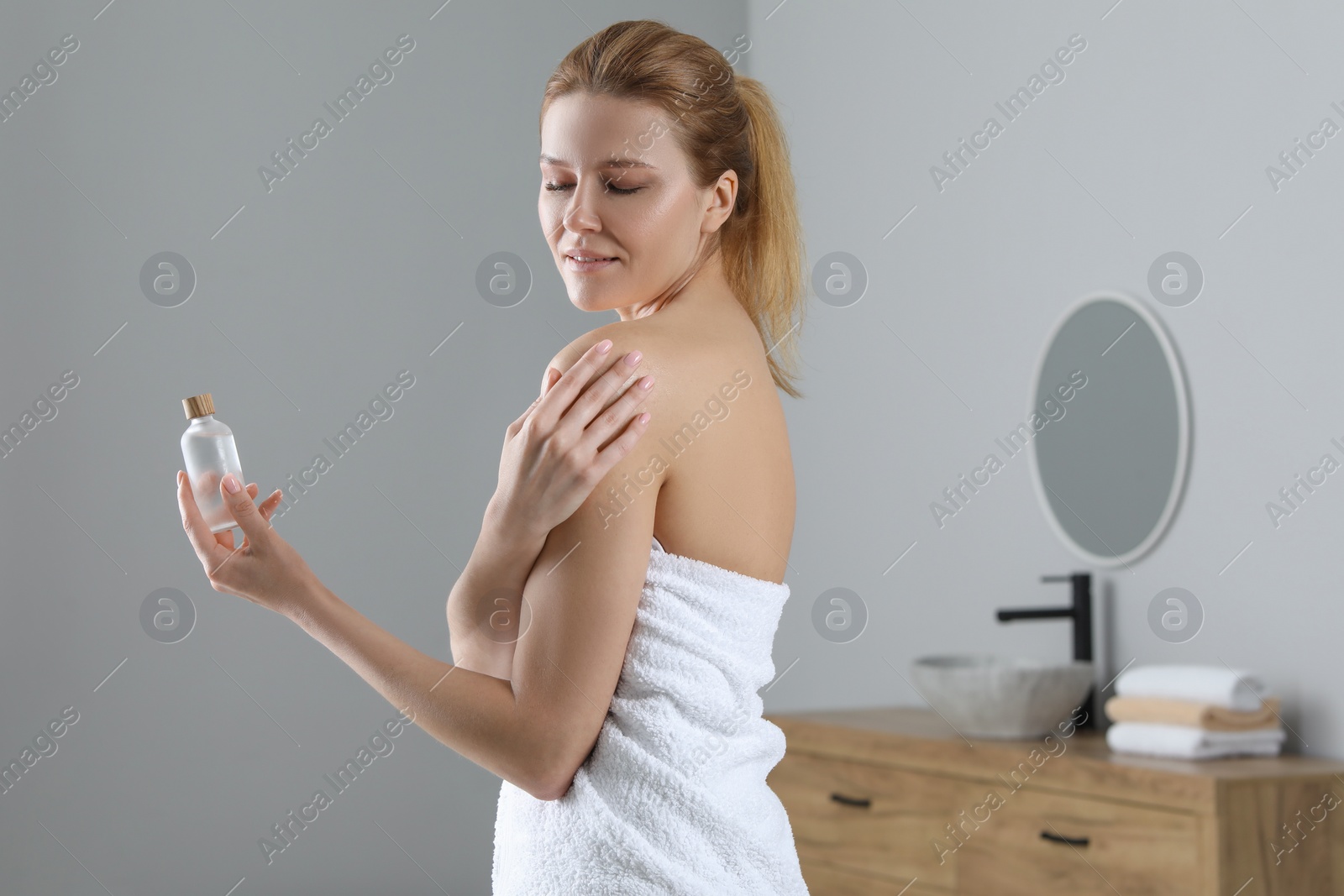 Photo of Beautiful woman applying body oil onto shoulder in bathroom