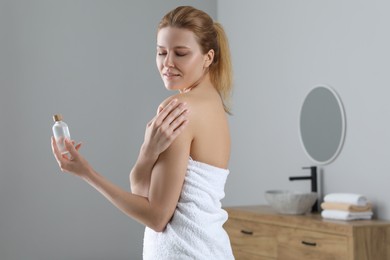 Beautiful woman applying body oil onto shoulder in bathroom