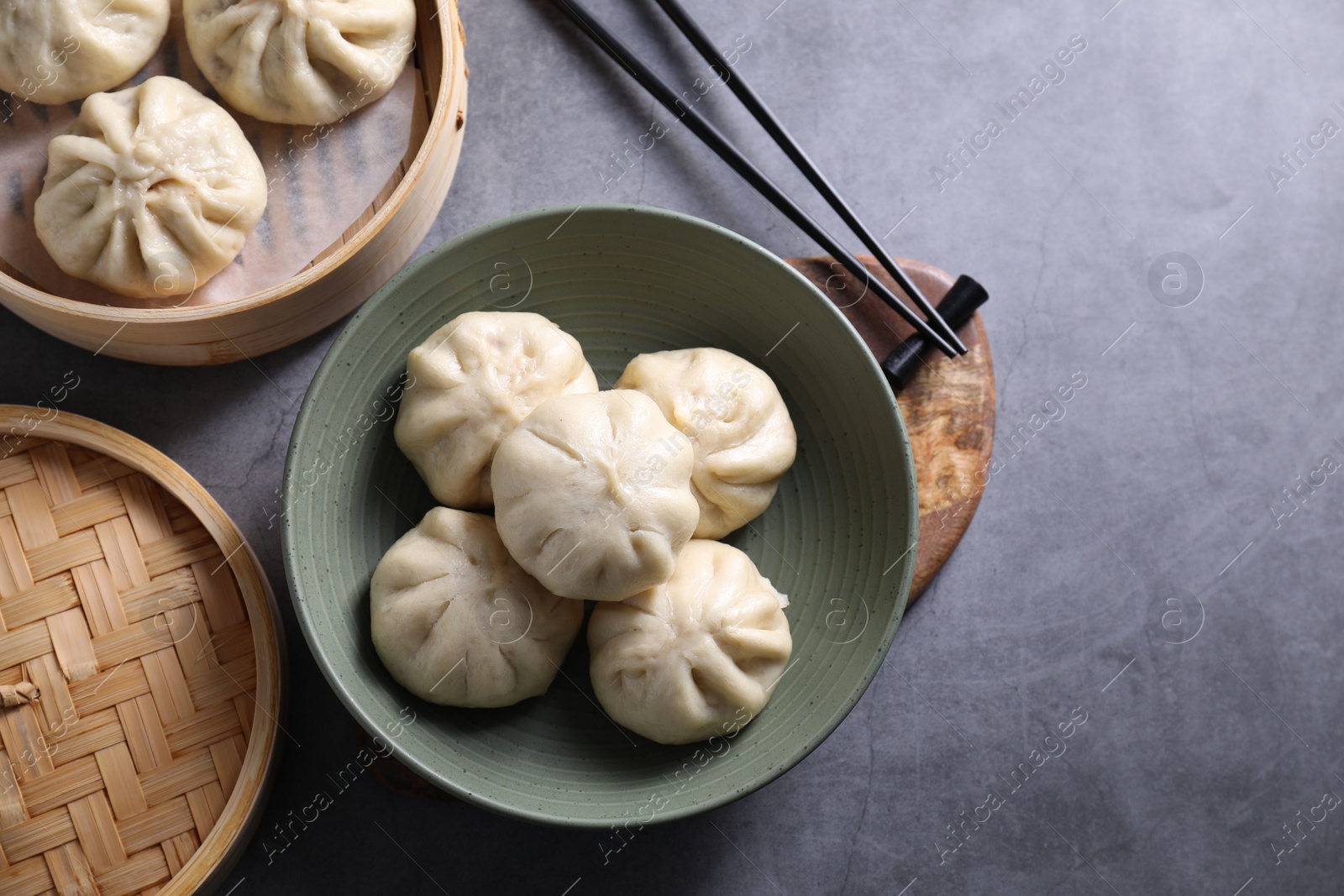 Photo of Delicious bao buns (baozi) and chopsticks on grey table, flat lay. Space for text