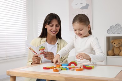 Photo of Motor skills development. Mother helping her daughter to play with colorful wooden arcs at white table in room