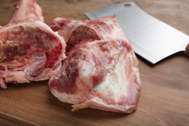 Photo of Cutting board with raw chopped meaty bones and butcher knife on wooden table, closeup