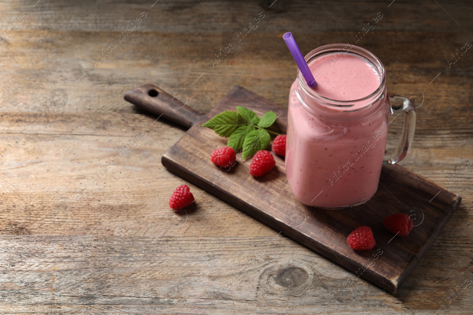 Image of Yummy raspberry smoothie in mason jar on wooden table. Space for text