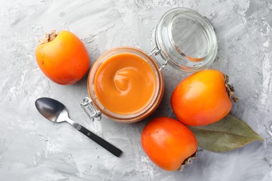 Delicious persimmon jam and fresh fruits on grey table, flat lay