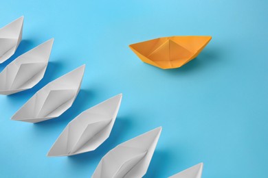 Photo of Yellow paper boat floating away from others on light blue background. Uniqueness concept