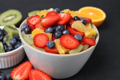 Delicious fresh fruit salad in bowl and ingredients on dark table, closeup