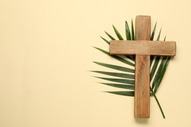 Photo of Wooden cross and palm leaf on beige background, top view with space for text. Easter attributes