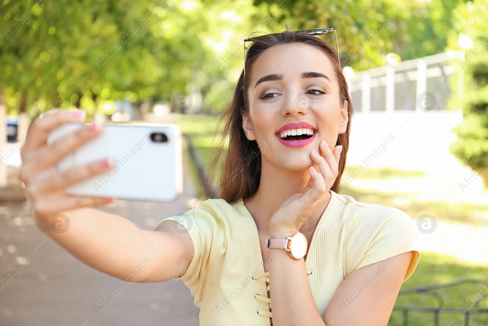 Photo of Young woman taking selfie outdoors on sunny day