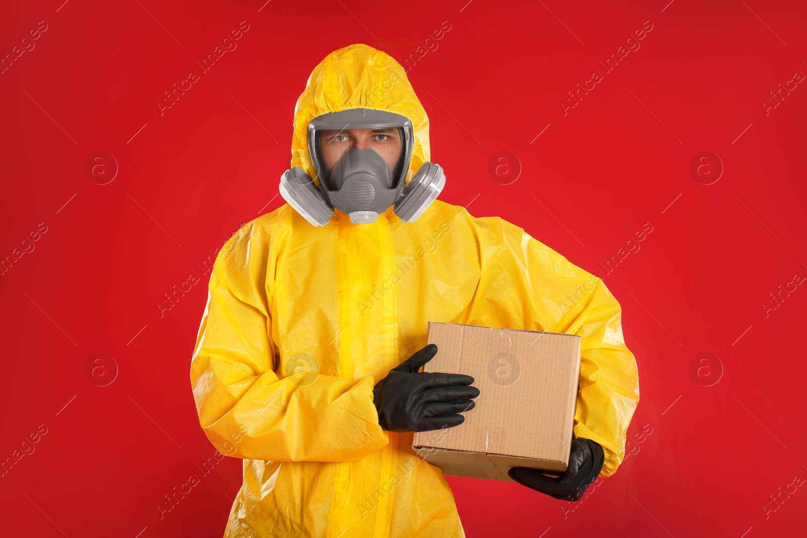 Photo of Man wearing chemical protective suit with cardboard box on red background. Prevention of virus spread