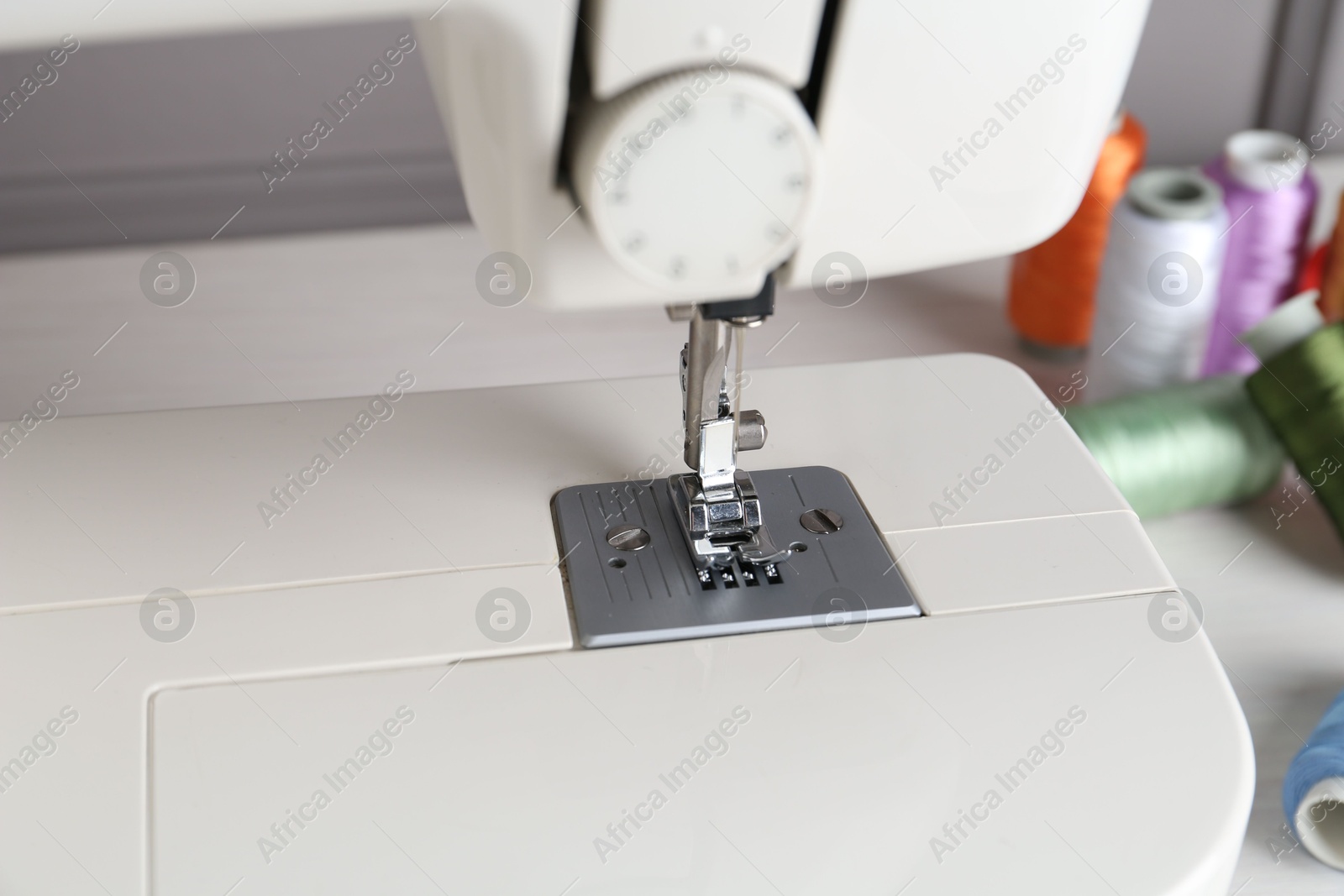 Photo of Sewing machine and spools of threads on white table, closeup