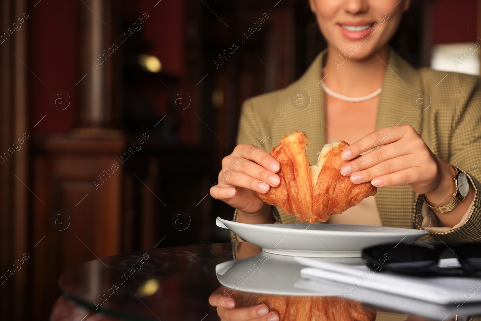 Photo of Woman breaking tasty croissant at table in cafeteria, closeup. Space for text