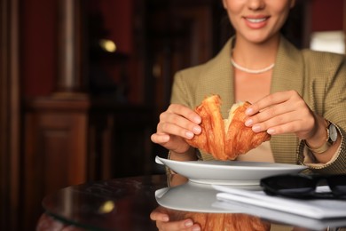 Photo of Woman breaking tasty croissant at table in cafeteria, closeup. Space for text