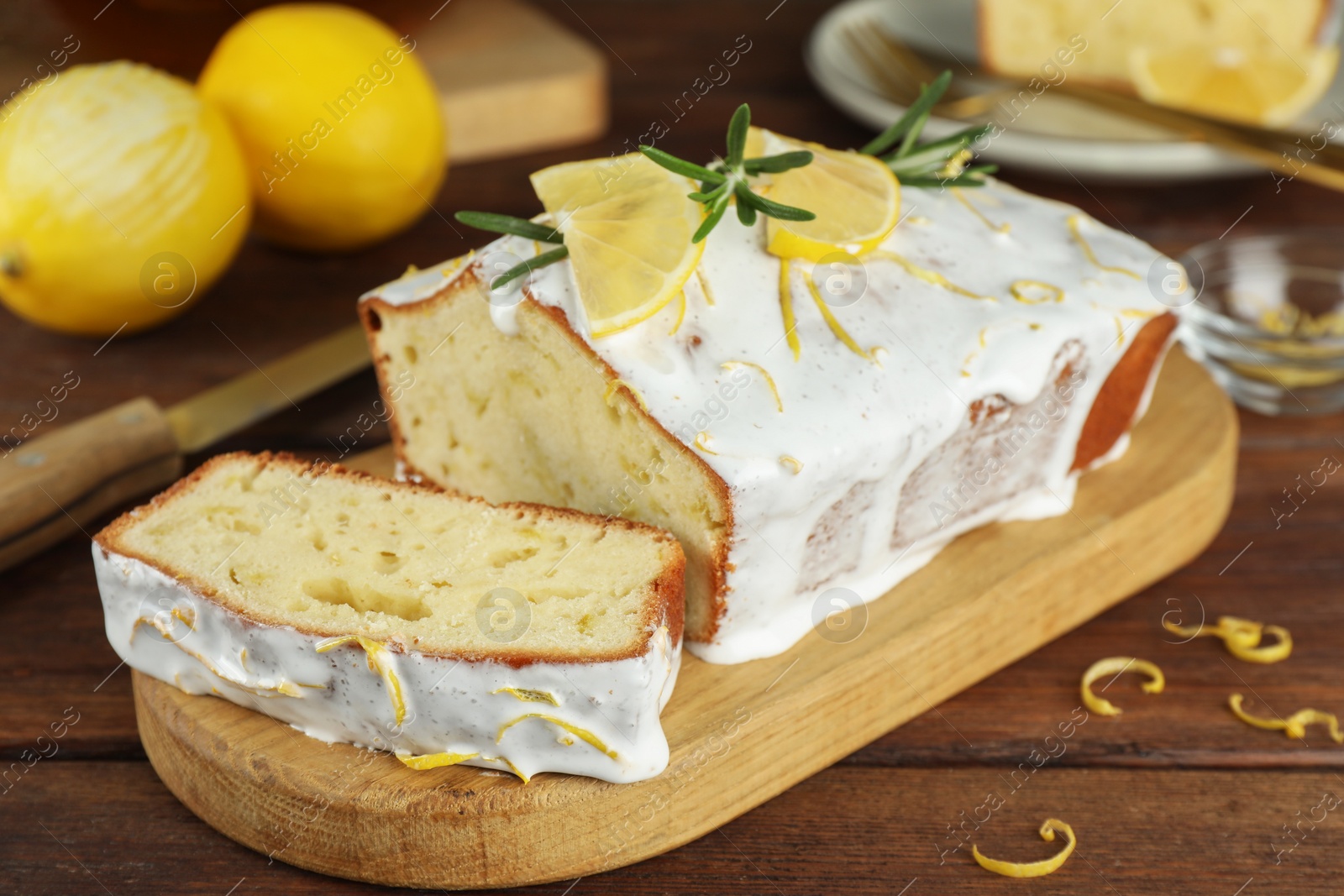 Photo of Tasty lemon cake with glaze and citrus fruits on wooden table, closeup